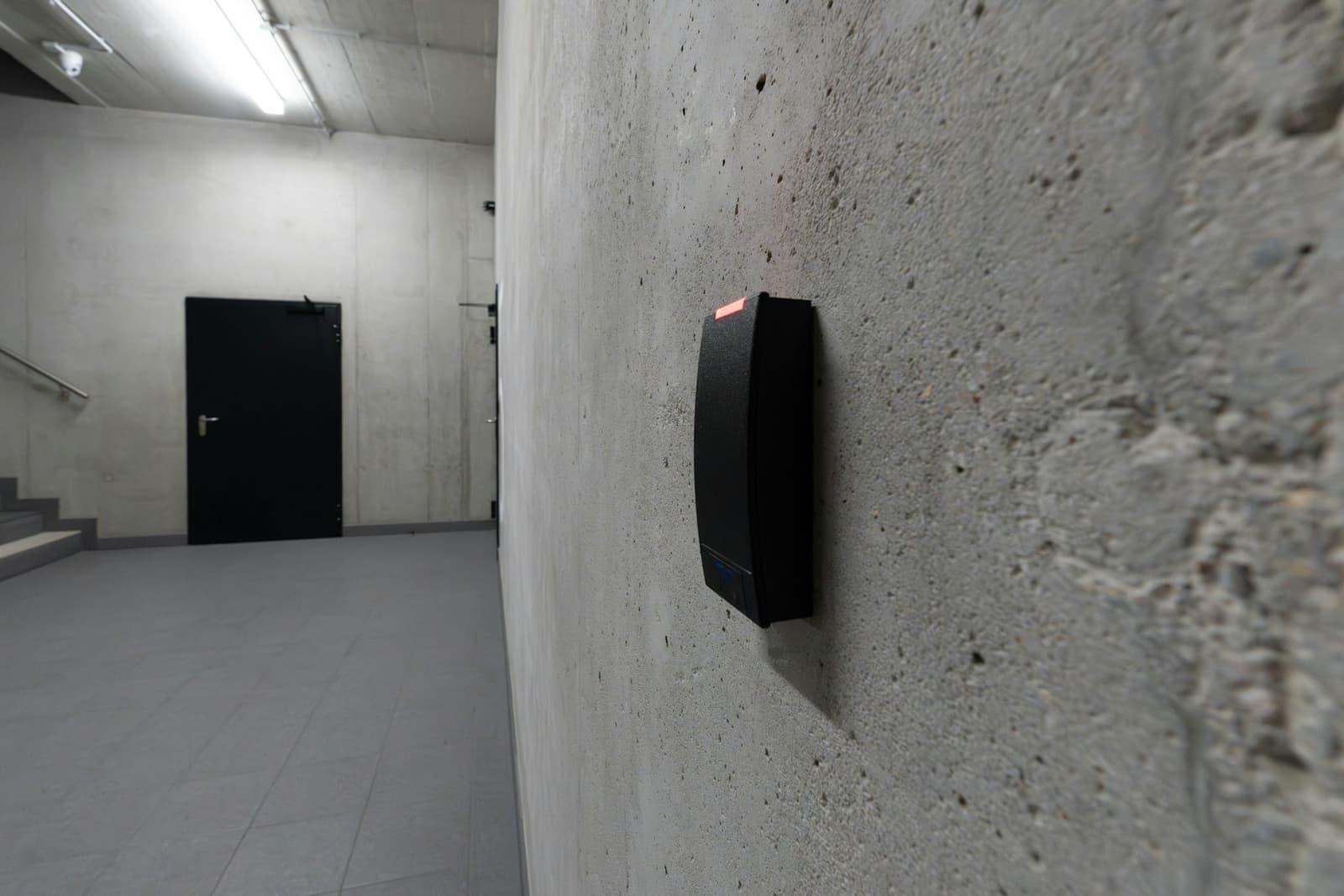 Lecteur de badge fixé sur un mur de béton, près d'une porte sécurisée.