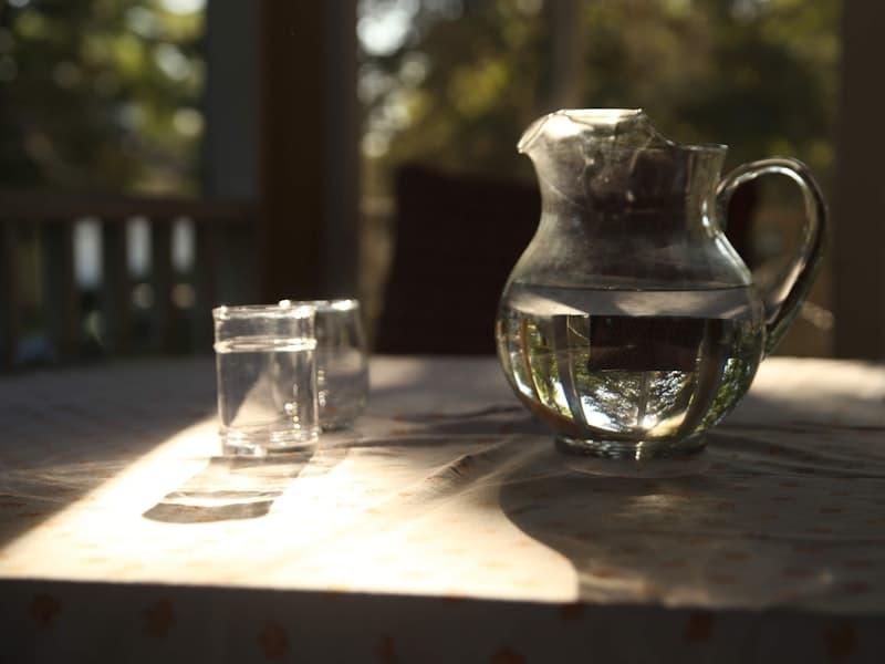 Carafe en verre et verres d'eau sur une table, à contre-jour.