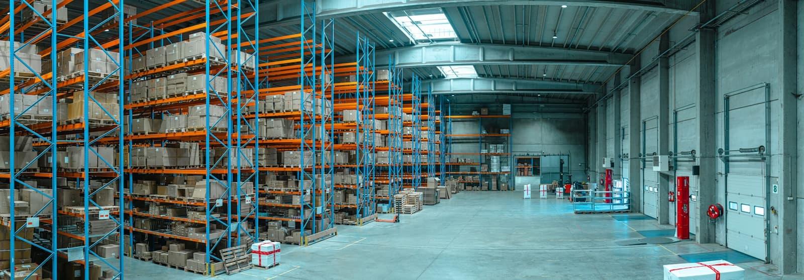 Allée d'entrepôt avec racks métalliques chargés de cartons.