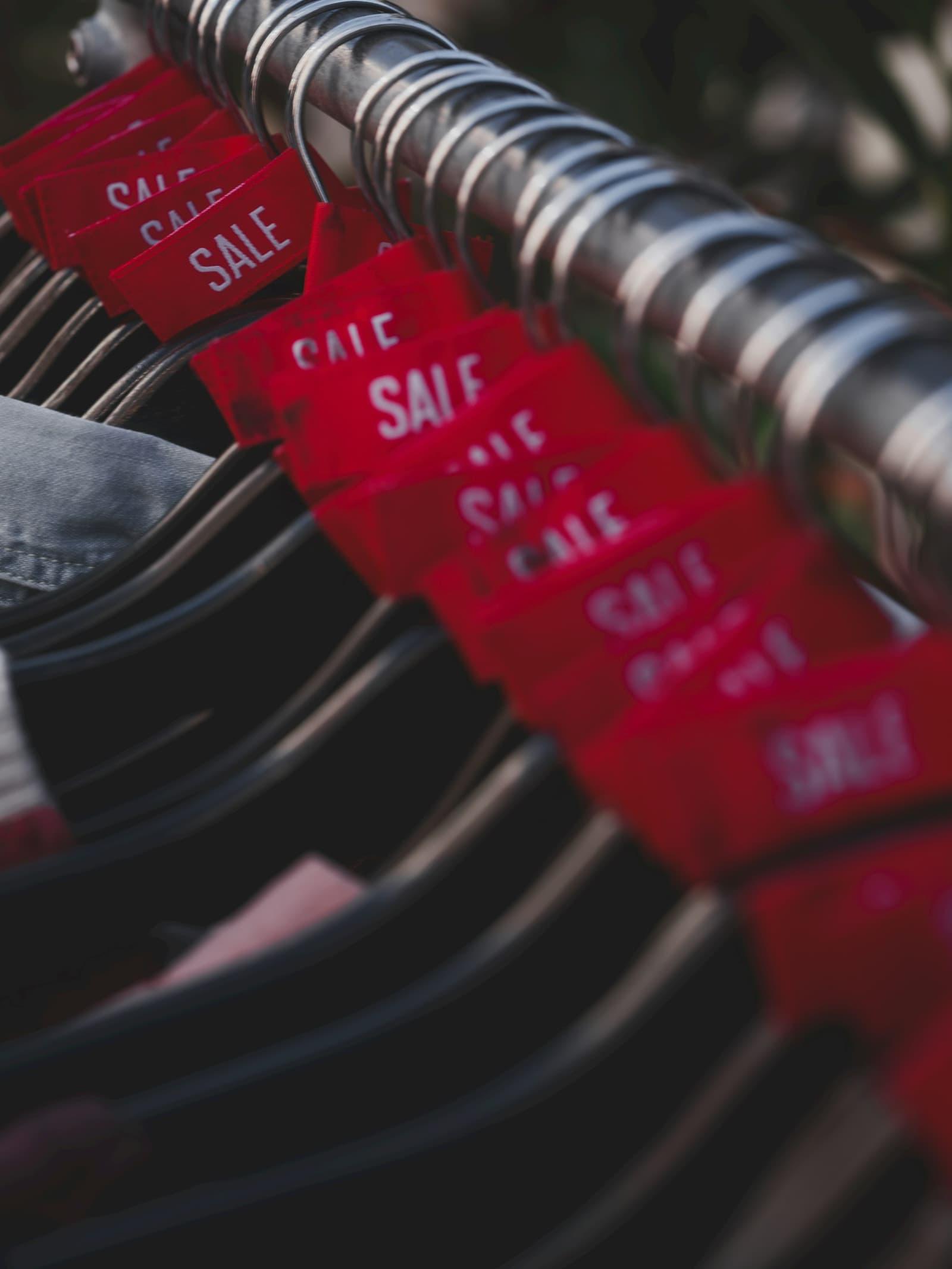 Étiquettes de soldes rouges accrochées à des cintres.