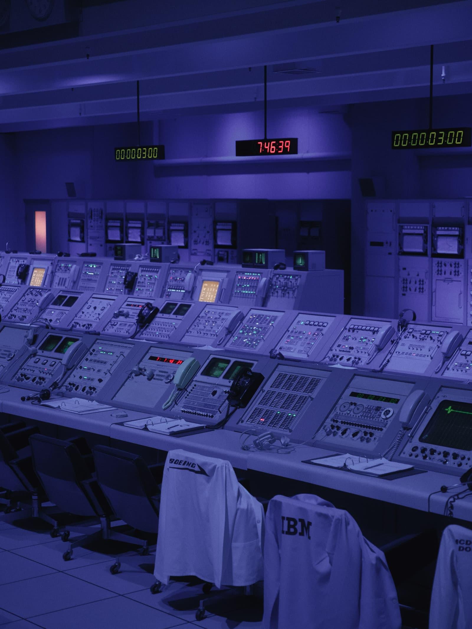 Longue console de postes de supervision sous une lumière bleue.